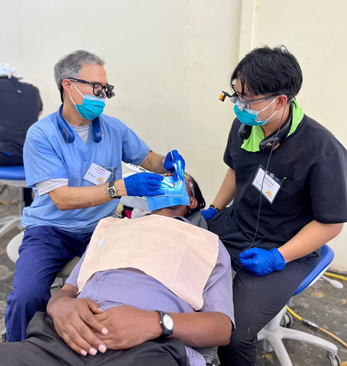 Dr Mark Stevenson (left), a dental practitioner with 34 years of experience, performs a root canal on a faculty member at William Knibb Memorial High School as part of the Great Shape! Inc. 1000 Smiles Mission, hosted at the school. Assisting him is Daniel
