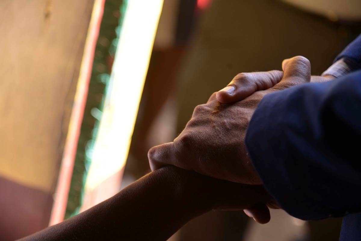 Prime Minister Dr Andrew Holness holds the hand of a grieving woman who lost her niece along the Commodore Road in Linstead, St Catherine, on October 6, where nine persons were shot by gunmen, five fatally on October 5. 