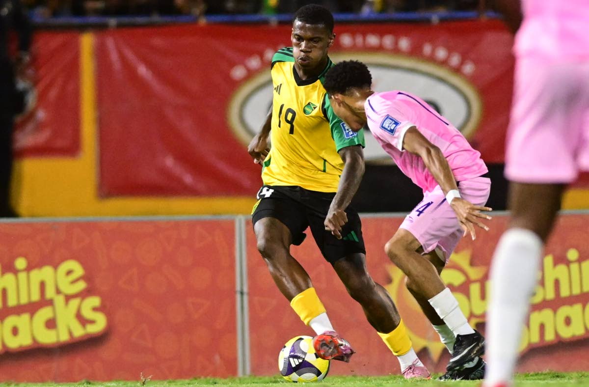 Regae Boyz’ Dujuan Richards (left) dribbles by Bermuda’s Deniche Hill during their Group B Concacaf World Cup qualification football match at the National Sadium yesterday. Richards scored the final goal in Jamaica’s 4-0 win.