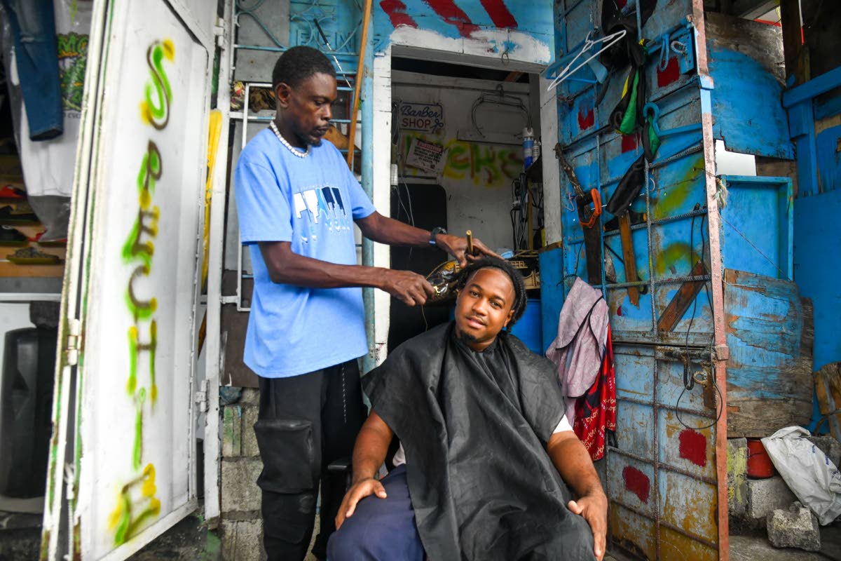 Barber and shop operator Vivian Andrews (left) trims his customer David Woodbine, a bus conductor, amid the rain and impending Hurricane Melissa at Andrews’ establishment on Beckford Street in Kingston yesterday.