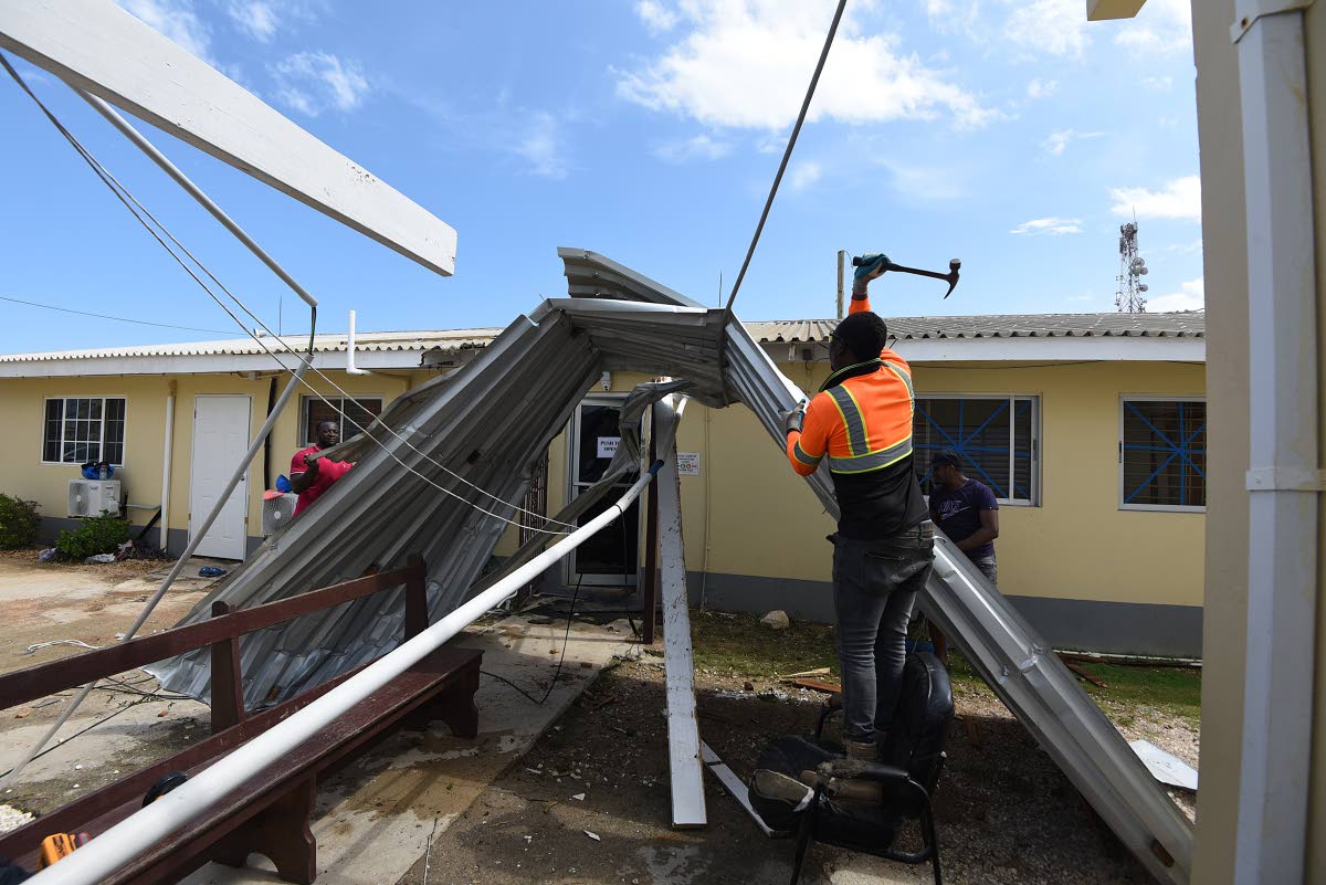 A worker tries to remove a zinc sheet that was entangled on a wire at the Falmouth Hospital in Trelawny after several roofs were blown off during the passage of Hurricane Melissa.