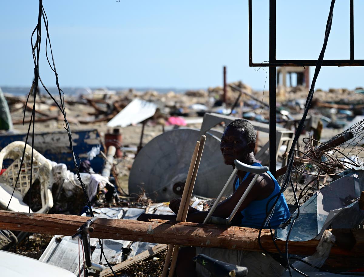 In this October 30 photo a man is seen sitting by the roadside on High Street, Black River, surrounded by debris of structures damaged by Hurricane Melissa.