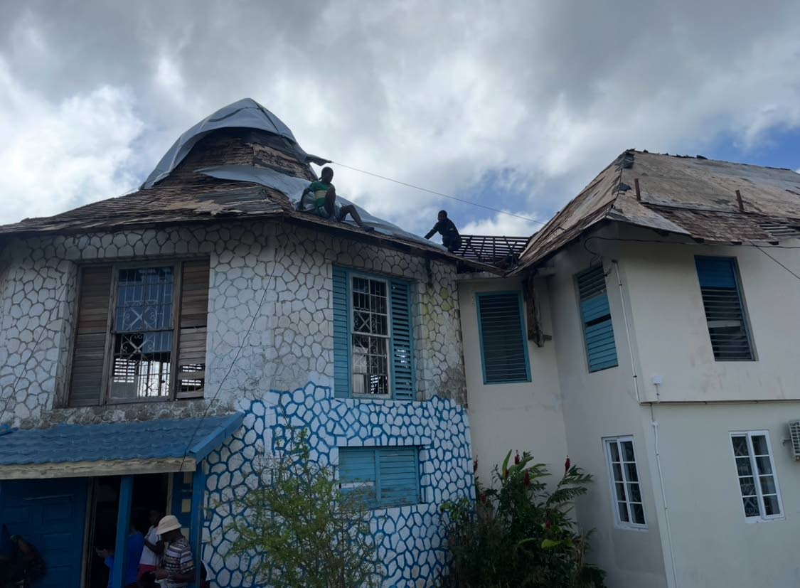 A civilian (left) and a policeman affixing a tarpaulin to the roof of the Montego Hills Police Station in St James.