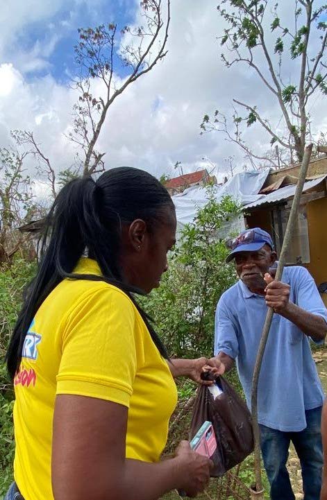 RJRGLEANER volunteer Susan Grant hands a care package to Lloyd Chambers of Marley Land Street in Lima, St James, whose tarpaulin-covered home reflects the toll of Hurricane Melissa.