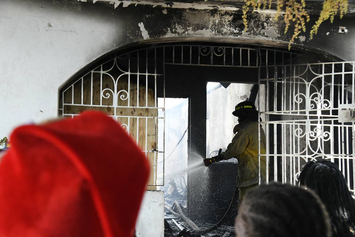 A firefighter conducts a cooling-down exercise on a five-bedroom house on Mountain View Avenue in St Andrew, which was one of three homes destroyed by fire on Thursday.