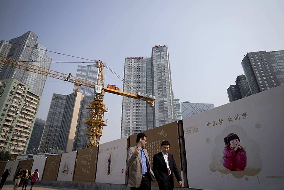 In this October 8, 2013, file photo, office workers walk past ‘China Dream’ message boards at a construction site.