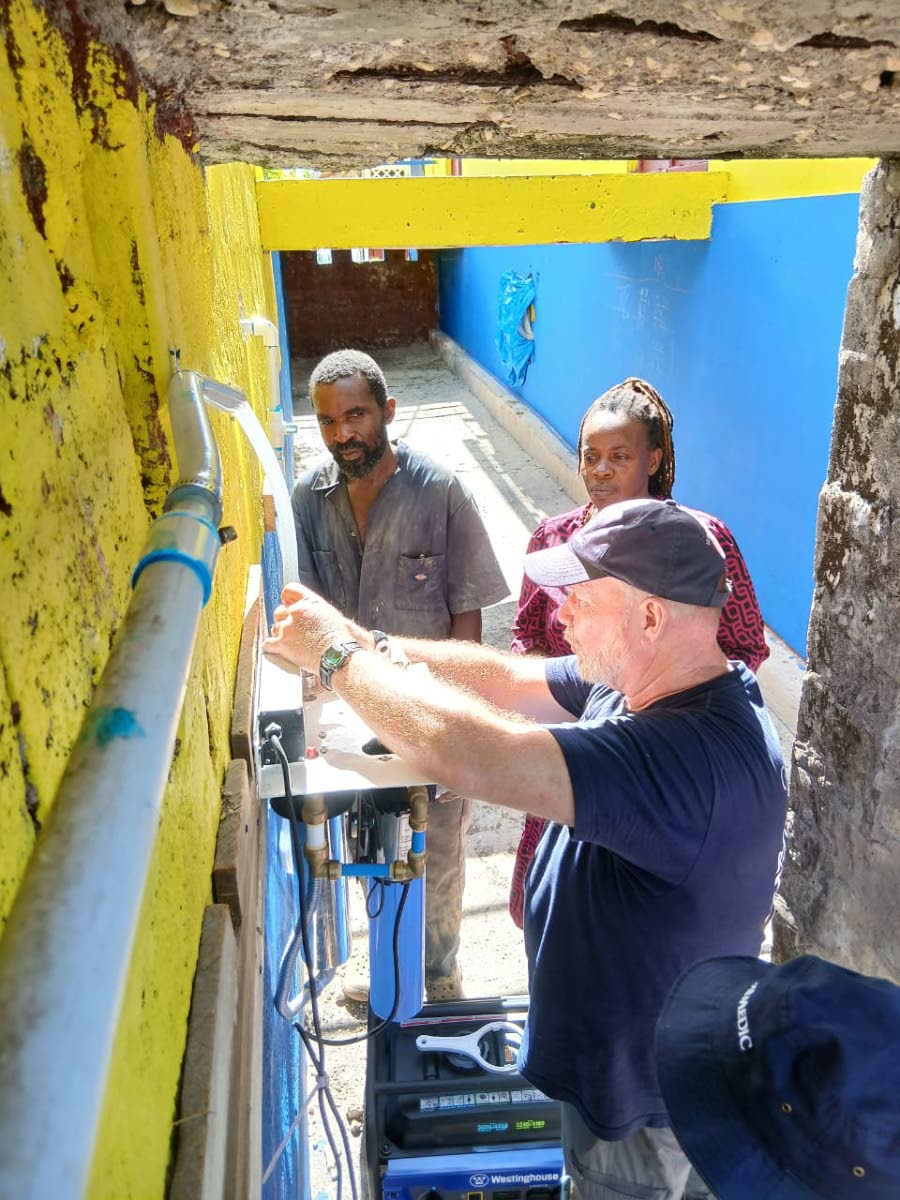 Murray and Ashley McKenzie, school groundsman and janitor, watch closely as Don Jorgensen, rapid response team leader for Global Medic, works on the UV water filter.
