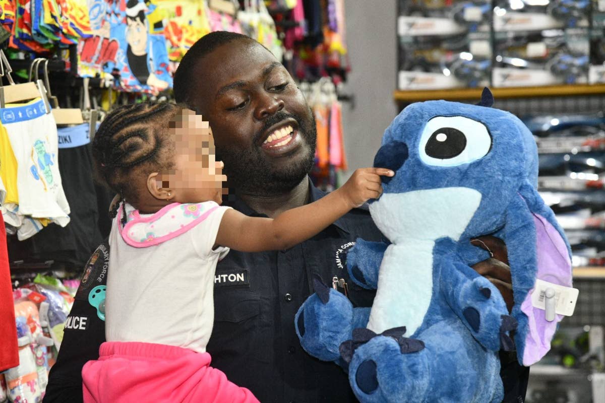 Superintendent of Police Throyville Haughton, attached to the St Catherine South Police Division, shares a warm moment with an infant as he presents her with a stuffed toy during the Shop with a Cop initiative.