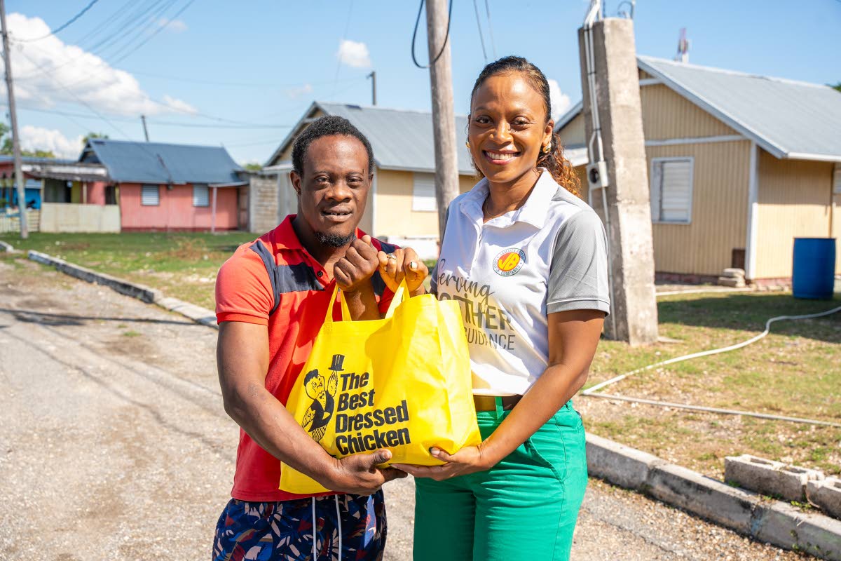Michelle Lawe (right), group human resources manager, Jamaica Broilers Group presents special Christmas package filled with groceries and The Best Dressed A-Grade whole chicken to Rashawn Johnson (left), at recent outreach initiative in McCook’s Pen.