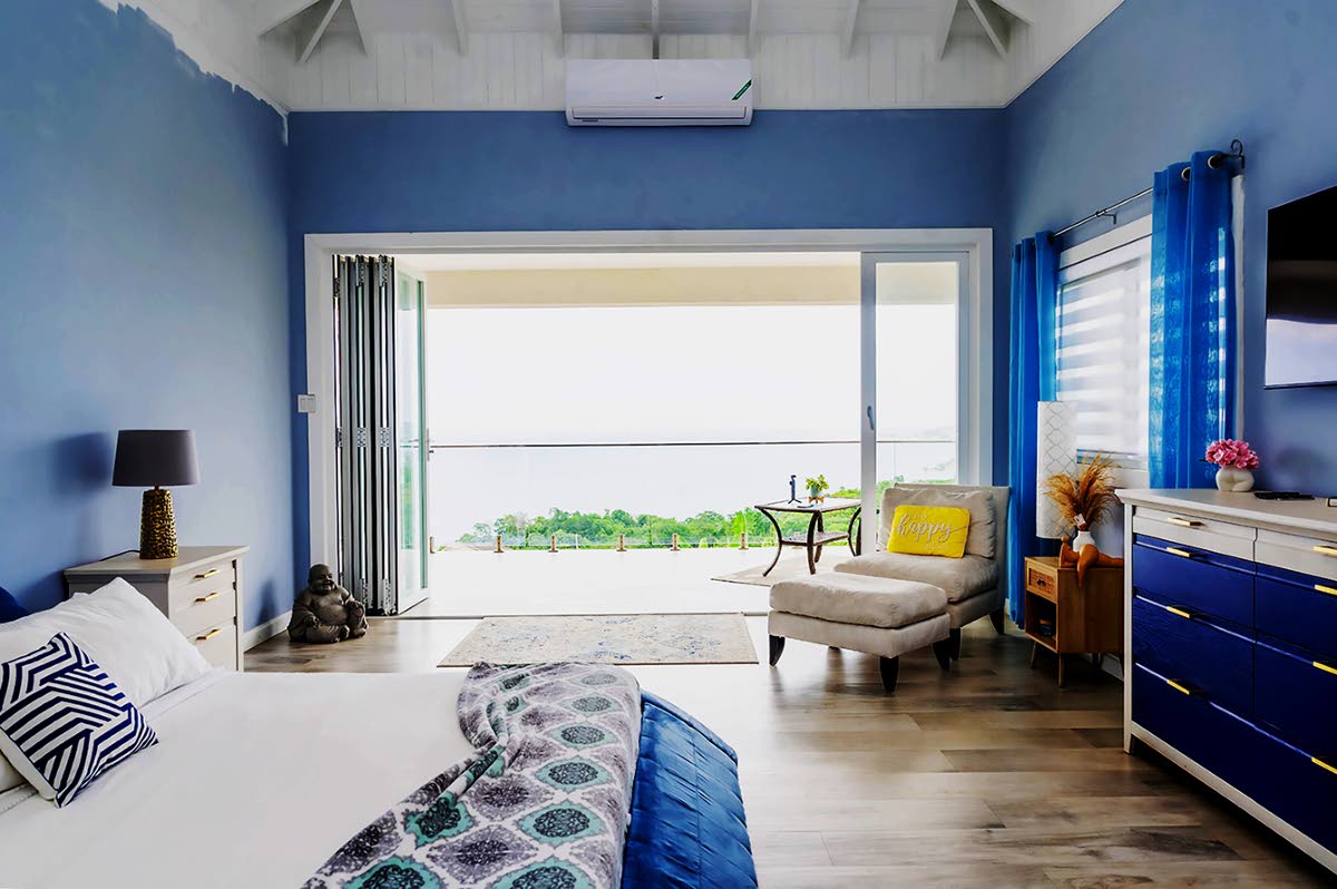 A restful primary bedroom in blue forges a bond with the hypnotic waterfront at Darlene Rhoden’s St James dream home.