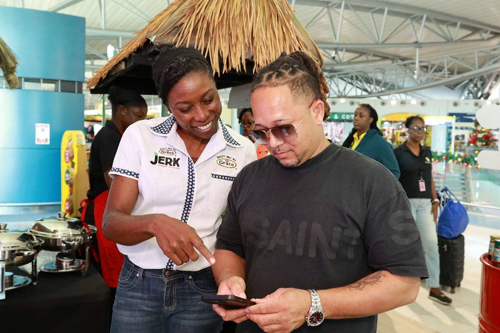 Sabrina Watson (left), global category manager – seasonings, sauces and spices at Grace Foods, guides traveller Richard Ho-sing in navigating the donation site at the Norman Manley International Airport during the Bring Jamaica Home activation.