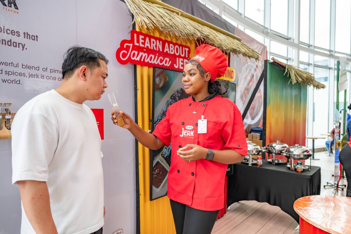  Winland Chang (left) indulges in the scent of original Jamaican spices. Engaging him is Brand Ambassador Jodian Willie at Grace’s Bring Jamaica Home Airport Pop Up at the Donald Sangster International Airport in Montego Bay, St James. 