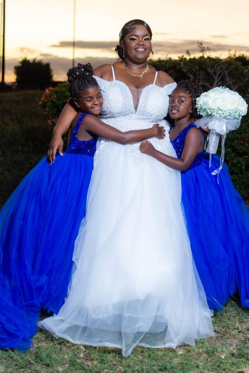A reflection of timeless style, the beautiful bride is flanked in a loving embrace by her flower girls Denoiya Walcott (left) and Makaylia Wilson.
