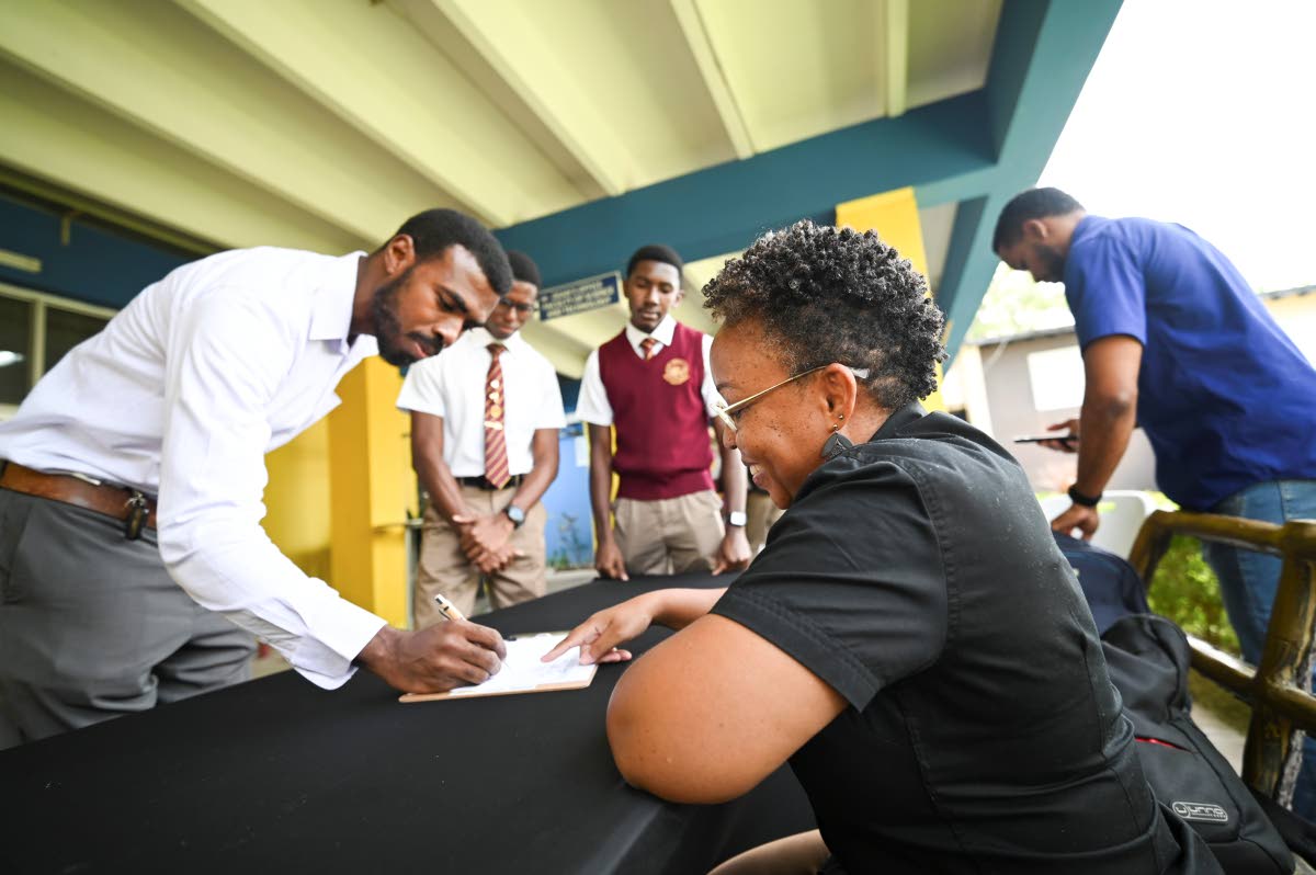 Wolmer’s Boys chemistry teacher Rashaan Smith (left) signs in to register his pupils for the CAPE/STEM workshop at the direction of JPS Foundation Officer Samora Bain, as Wolmer’s students Ajani Banjoko (right) and Jabari Royal look on.
