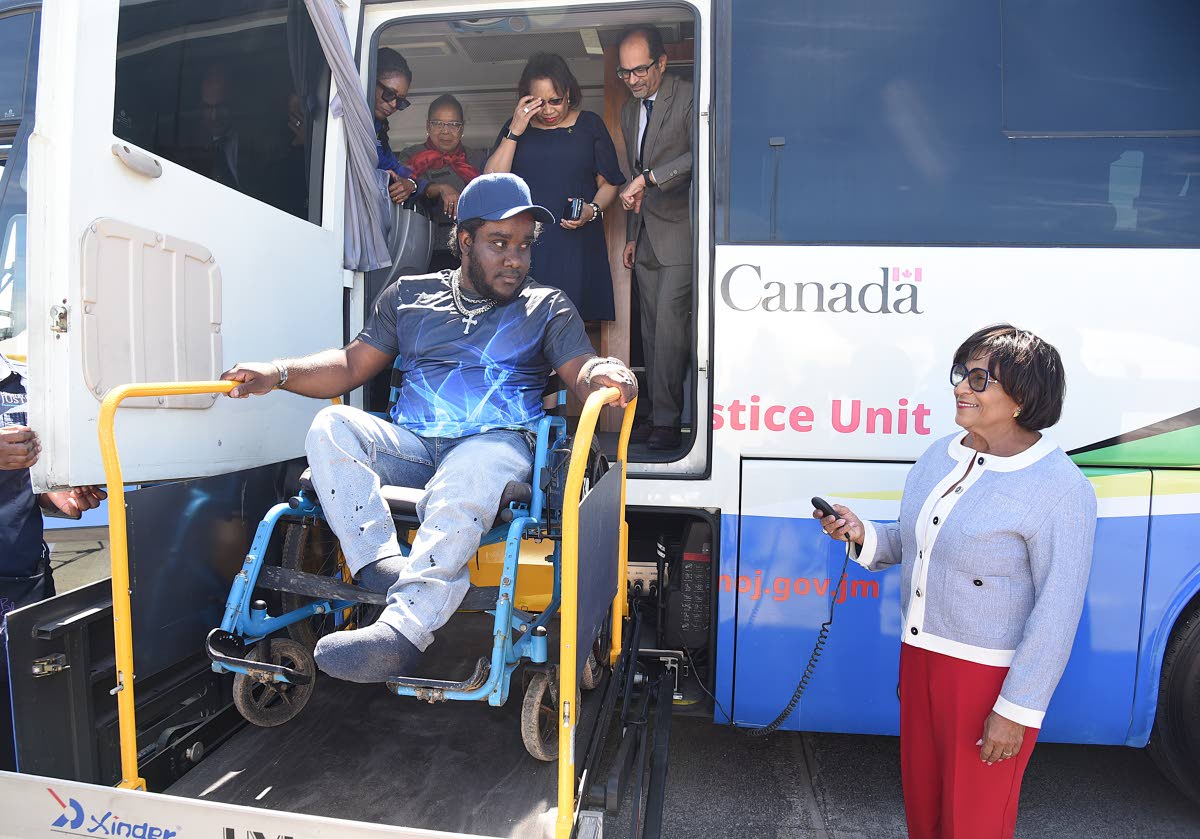 Leco Bradford smiles as Marisa Dalrymple‑Philibert (right), minister of state in the Ministry of Justice and Constitutional Affairs, operates the lift to assist him on to the Justice Bus. Looking on are Dian Watson (left), executive director of the Legal