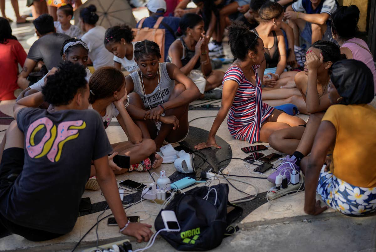 Residents charge their electronic devices on a street during a general blackout in Havana, Saturday, March 15, 2025. 