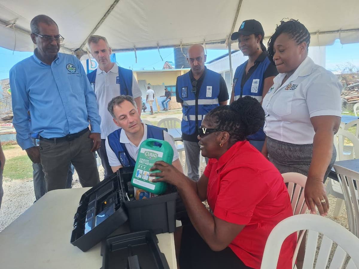 Alexander De Croo (seated), administrator of the United Nations Development Programme (UNDP) and United Nations under-secretary-general, interacts with Keisha Wint, a blind poultry farmer from South Manchester, as she displays her first aid kit presented t