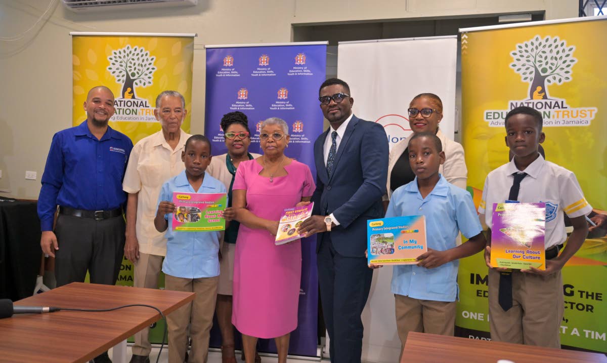 Carlong Publishers chair, Shirley Carby (centre), presents Fitzroy Abbott, principal of Christiana Moravian Primary and Infant School in Manchester, with a copy of one of the textbooks donated by the company. Joining them are (from left) Carlong Publishers