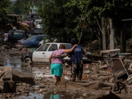 A Marine helps a woman cross a flooded street in Poza Rica, Veracruz state, Mexico, Sunday, October12, 2025. (AP Photo/Felix Marquez)