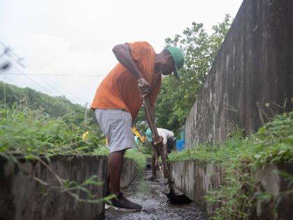 Workmen labour to clear debris from drains along the Race Course main road in St Mary on Monday.