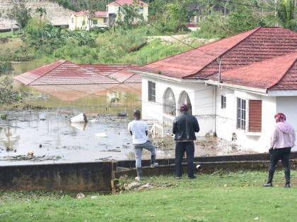 Onlookers view houses and motor vehicles that were left submerged on Gibson Close in Mandeville, Manchester, after the passage of Hurricane Melissa.