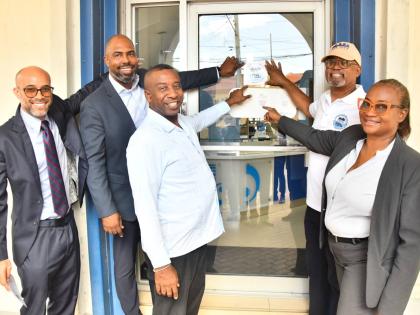Michael McMorris (second right), chair of the Downtown Kingston Redevelopment Initiative Committee, affixes the decal on the door of Imperial Optical Broadbent on Duke Street. Sharing in the moment on Wednesday are (from left) Jonathan Swire, second vice-p