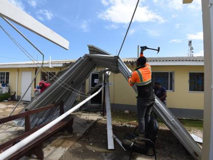 A worker tries to remove a zinc sheet that was entangled on a wire at the Falmouth Hospital in Trelawny after several roofs were blown off during the passage of Hurricane Melissa.