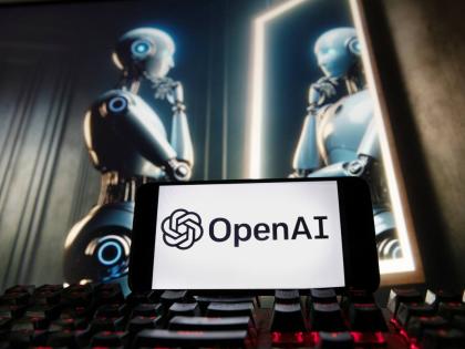 The OpenAI logo is displayed on a cellphone with an image on a computer monitor generated by ChatGPT’s Dall-E text-to-image model.