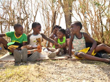 Children sit by the roadside, smiling amid the devastation of their community in Oxford, St Elizabeth, after Hurricane Melissa.