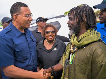 Prime Minister Dr Andrew Holness (left) with Chief of the Accompong Maroons in St Elizabeth, Richard Currie, during a visit to the community. Olivia Grange, minister of culture, gender, entertainment and sport, looks on.
