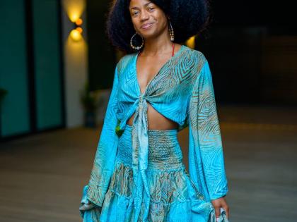 Web Designer, Samiyyah Andrewin-Miranda, stuns in a flowing turquoise outfit featuring a tie-front top with billowy sleeves and a smocked waist, paired with a tiered skirt that adds movement to the look.