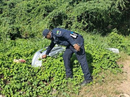 Senior Superintendent Hopeton Nicholson, head of the St Catherine North Police, retrieves a motor-vehicle bumper from bushes during a raid at a premises off St John's Road in Spanish Town on December 12, 2025. 
