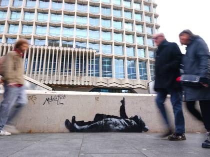 Pedestrians walk past a graffiti artwork, depicting two people, outside Tottenham Court Road Station in London, Monday, December 22, 2025 as elusive street artist Banksy appeared to confirm Monday that an identical image appeared on a wall on the side of a