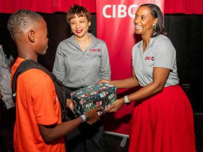 CIBC Caribbean’s Head of Country, Annique Dawkins and Sherian McDonald, senior manager deals management, present gifts to a ward of the state at the United Way of Jamaica’s annual ‘Bringing Cheer to Children in State Care’ initiative.