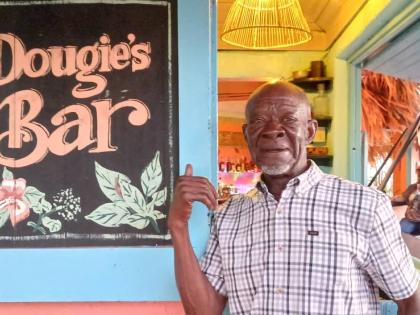 Douglas ‘Dougie’ Turner pointing to the sign of the bar that was named in his honour at Jakes Treasure Beach in St Elizabeth.
