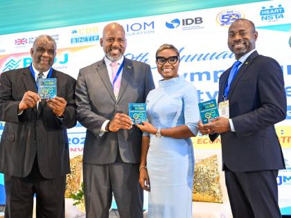 Minister of State in the Ministry of National Security and Peace, Juliet Cuthbert-Flynn, is presented with a copy of the ‘Living in Jamaica: A Guide to Services and Support’ handbook by Director General of the Planning Institute of Jamaica (PIOJ), 