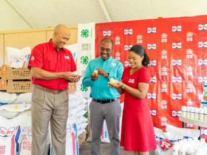 Retired Colonel Jaimie Ogilvie (left), vice president of Hi‑Pro; Peter Thompson (centre), executive director of Jamaica 4‑H Clubs; and Sherrae Wong‑Black (right), Hi‑Pro farm store manager, share a light moment as they handle three of the 3,000 bab