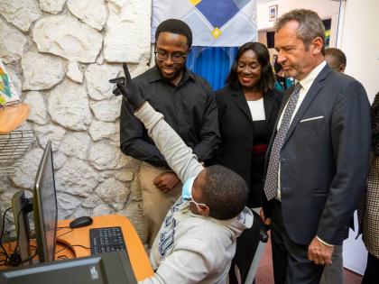 A Chetwood Memorial Primary School student uses a desktop computer as JLS Communications Director Royane Green (standing left), JLS Director General Maureen Thompson (centre), and UNESCO Caribbean Director Eric Falt (right) look on.