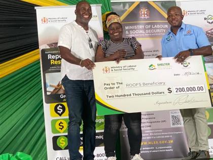 Sylvia Ferguson (centre) of Darliston, Westmoreland, beams as she receives a symbolic cheque valued at $200,000 under the Government’s Restoration of Owners or Occupants of Family Shelter (ROOFS) Programme, administered through the Ministry of Labour and