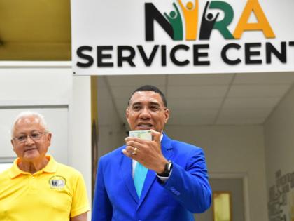 Prime Minister, Dr Andrew Holness (right), displays his national identification card during the official launch of the National Identification Registration Authority (NIRA) at the NIRA Centre, Central Sorting Office in Kingston. Looking on is Minister of J