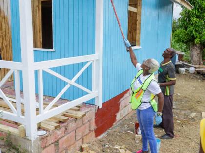 Sharon Williams, director, NCB Foundation, applies a final coat of paint as Hubert Samuels prepares to welcome his family back into their restored Black River home. 