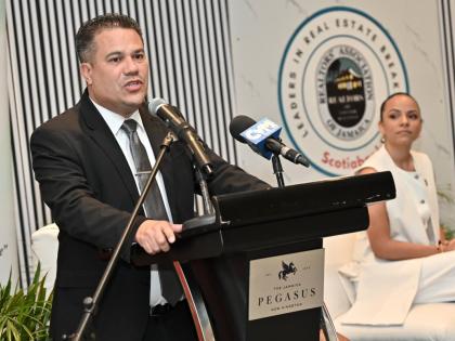 
Matthew Samuda, minister of water, environment, and climate change, speaks while Gabrielle Gilpin-Hudson, (right) president of Realtors Association of Jamaica, looks on at the Realtors Association of Jamaica Leaders in Real Estate Breakfast under the them