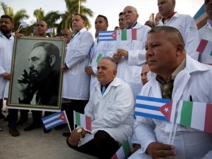 In this March 2020 photo, Cuban doctors and medical professionals pose for the media with a photo of Fidel Castro and flags of Italy and Cuba, prior to their departure to Italy to assist with the COVID-19 pandemic. 