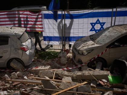 Israeli authorities hang Israeli and United States flags at the site struck by an Iranian missile that killed two people, in Ramat Gan, Israel on March 18, 2026. (AP Photo/Oded Balilty)