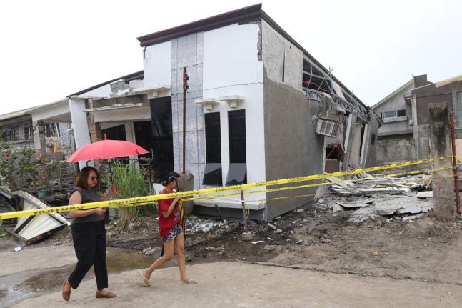 Two women walk past a damaged house after a strong earthquake in Davao City, southern Philippines on Friday October 10, 2025. (AP Photo/Manman Dejeto)