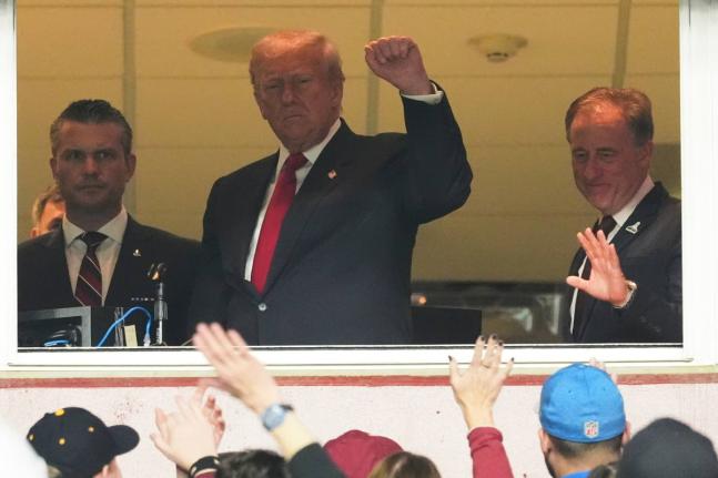 US President Donald Trump (centre) gestures to the crowd alongside Defence Secretary Pete Hegseth (left) and Washington Commanders owner Josh Harris, as they attend an NFL football game between the Commanders and the Detroit Lions at Northwest Stadium in L