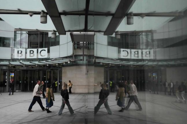 Pedestrians are reflected as they walk outside BBC Broadcasting House in London, Tuesday, November 11, 2025. (AP Photo/Kirsty Wigglesworth, file)
