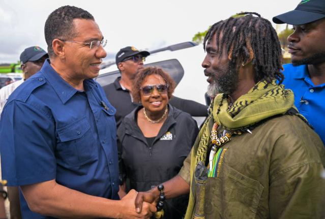 Prime Minister Dr Andrew Holness (left) with Chief of the Accompong Maroons in St Elizabeth, Richard Currie, during a visit to the community. Olivia Grange, minister of culture, gender, entertainment and sport, looks on.