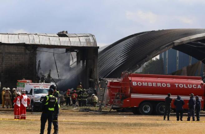 Firefighters and Red Cross workers tend to the site of a plane crash near Toluca airport in San Mateo Atenco, Mexico, Monday, December 15, 2025. (AP Photo/Ramses Mercado)