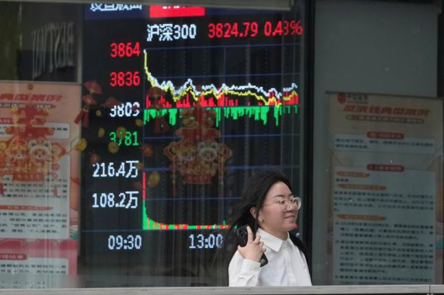 AP
A woman passes by a stock index at a brokerage in Beijing in May 2025. 